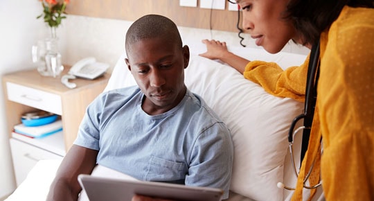 Man in hospital bed reviewing a tablet with a staff member